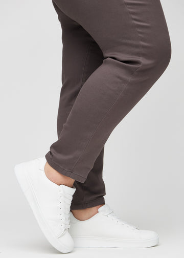 Slim jeans for women in grey-brown, color Thunders. Close-up at the ankles on a plus-size model, showing the fit at the leg openings.