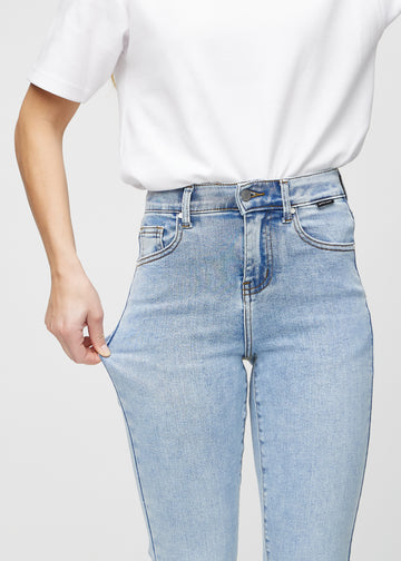 Slim jeans for women in light blue, color Waves. A model stretches the jeans at the thigh to show the fabric&