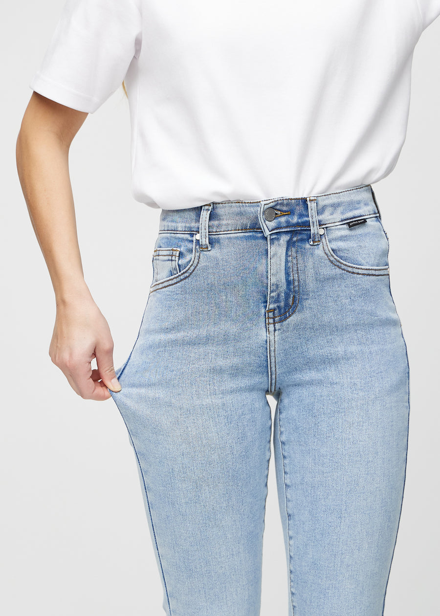 Slim jeans for women in light blue, color Waves. A model stretches the jeans at the thigh to show the fabric&