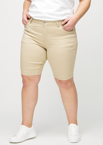 Beige skinny middle shorts, model name Gazelles, which fit snugly around the thighs and end just above the knee on a plus-size model, seen from the front.