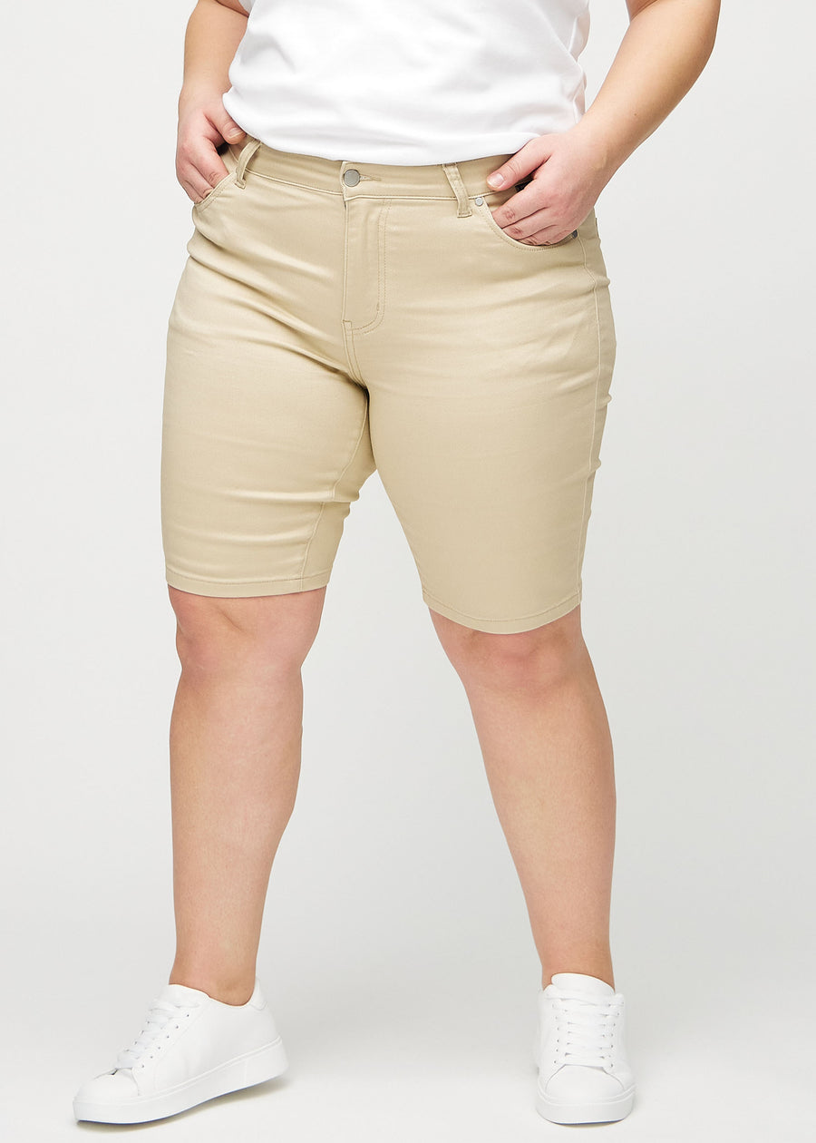 Beige skinny middle shorts, model name Gazelles, which fit snugly around the thighs and end just above the knee on a plus-size model, seen from the front.