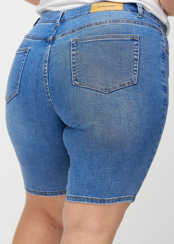 Denim skinny middle shorts seen from the back close up on a plus-size model to show details.