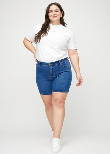 Full image of a plus-size model in dark denim skinny short shorts.