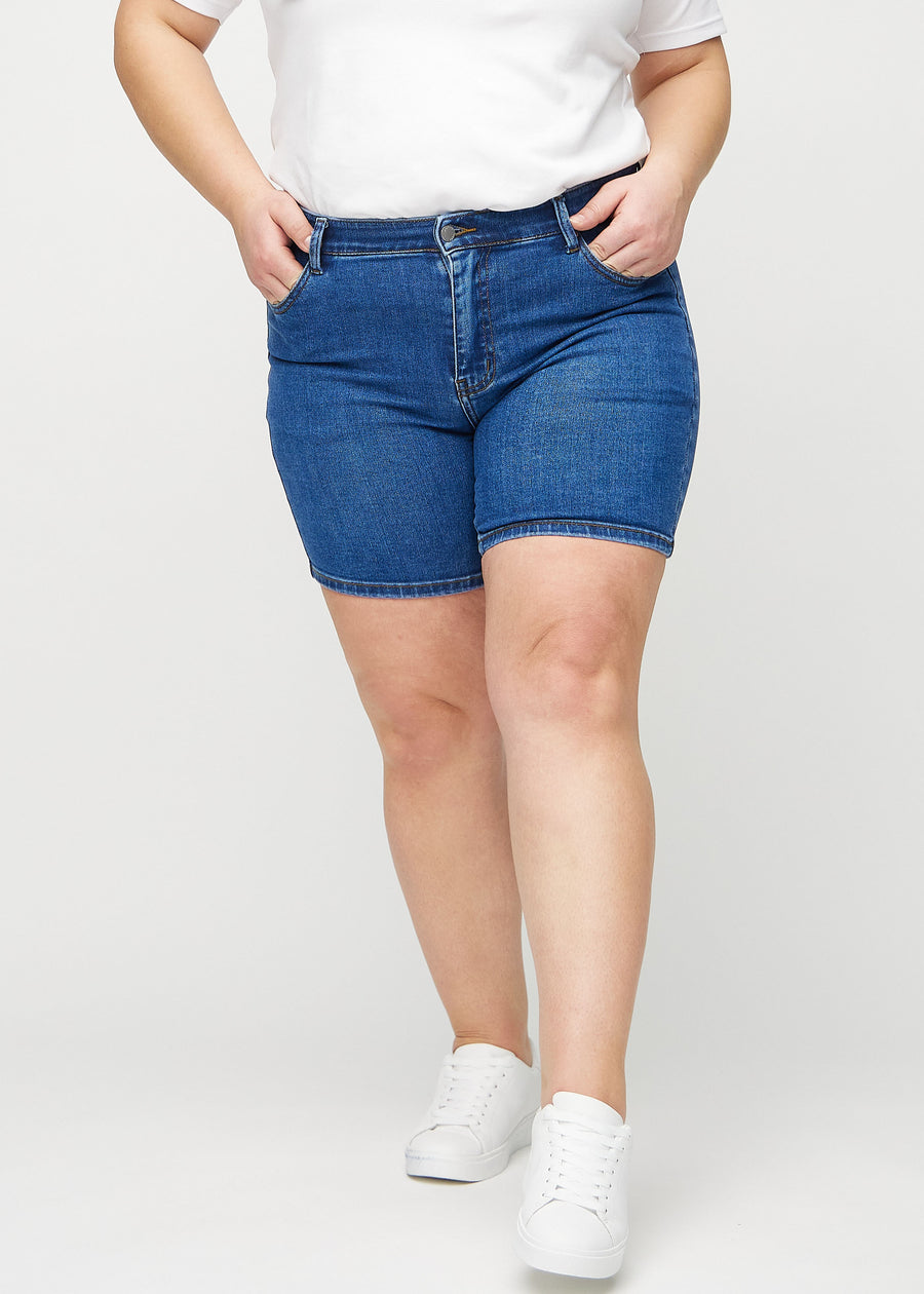 Dark denim skinny short shorts, model name Oceans, which are tight-fitting and end mid-thigh on a plus-size model, seen from the front.