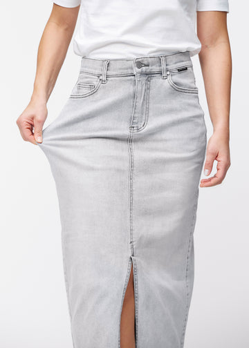 Long light grey denim skirt for women in the color Ashes. A model stretches the fabric at the hip to demonstrate its stretch.