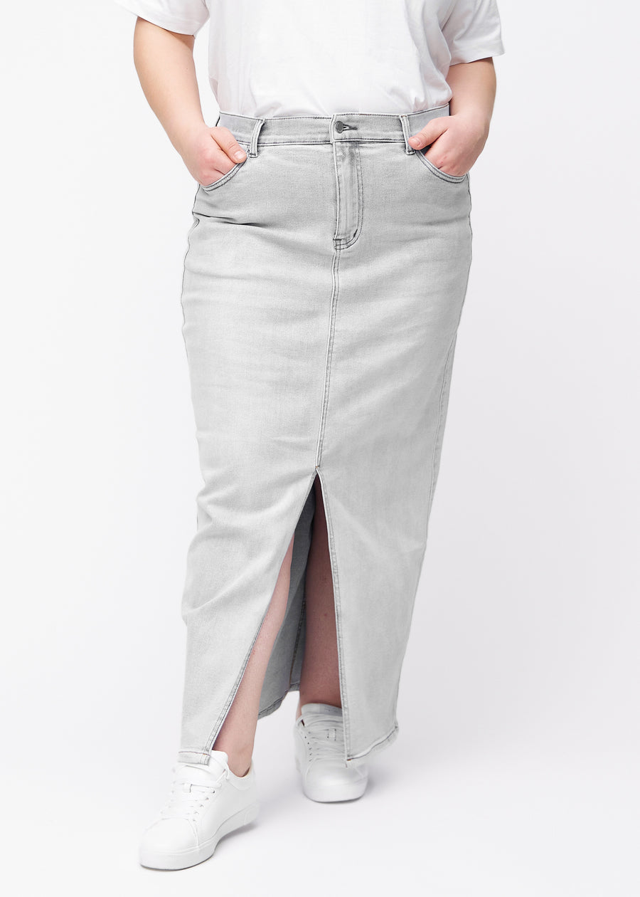 Long light grey denim skirt for women in the color Ashes. Front view on a plus-size model, showing the straight fit from the hips and a front slit starting below the knee.
