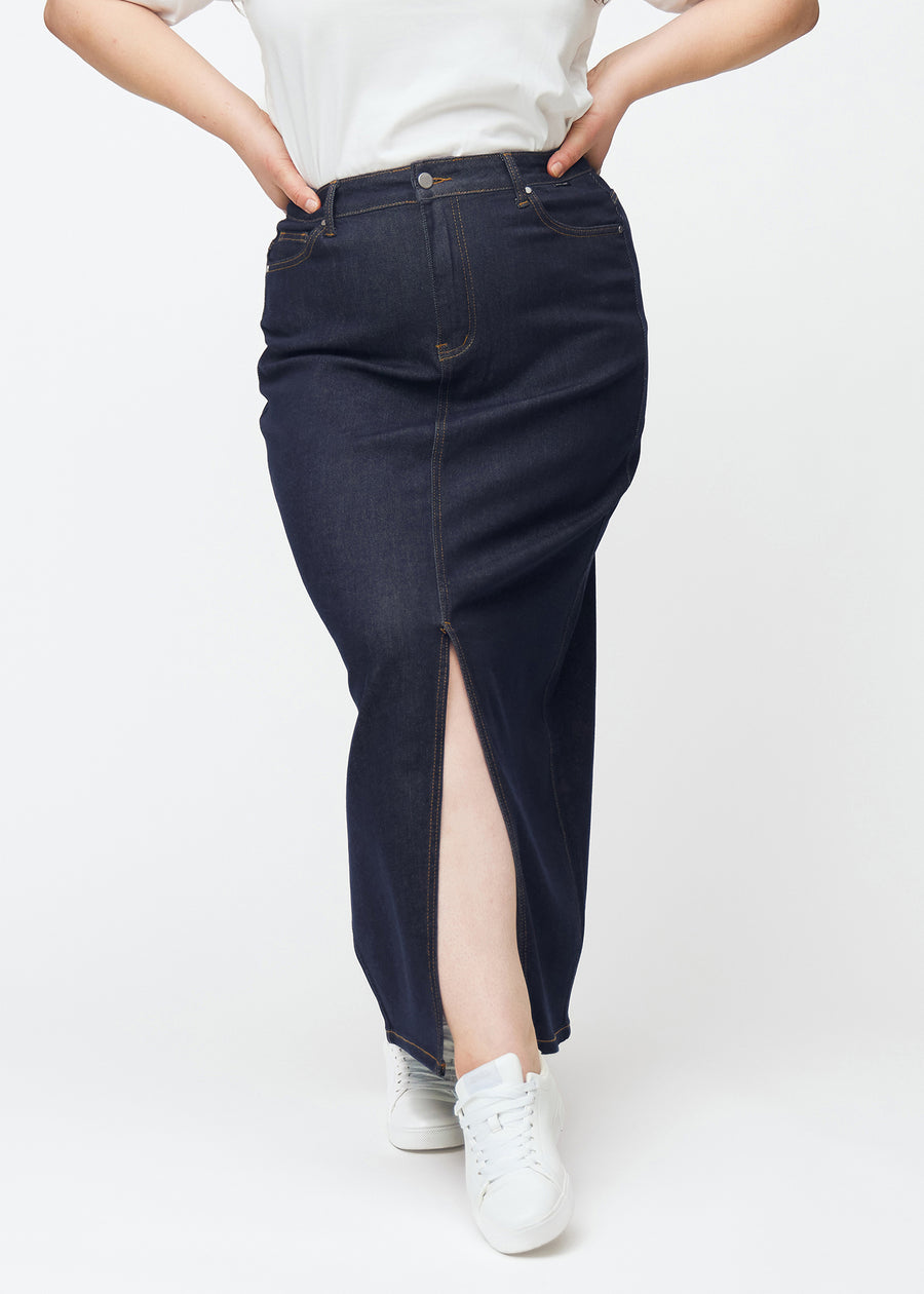 Long deep dark blue denim skirt for women in the colour Midnights seen from the front on a plus-size model, with a front slit starting just below the knee.