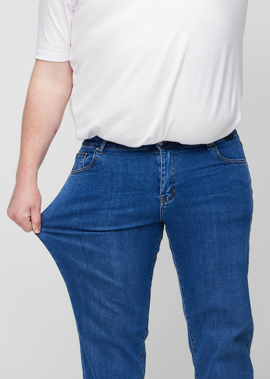The plus-size model stretches the jeans at the thigh to show the stretch.