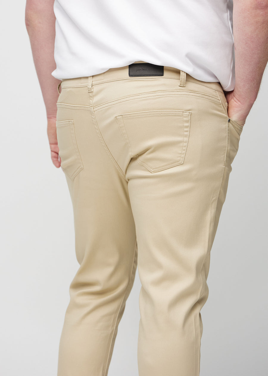 Close-up back view of beige slim jeans on a plus-size model showing details.