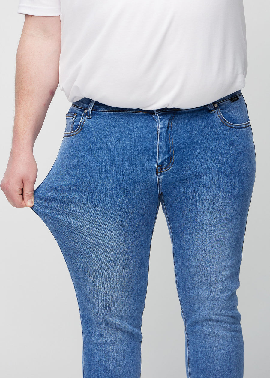 Plus-size model strækker jeansene ved låret for at vise stretch.