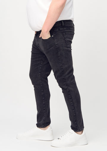 Dark grey denim slim jeans viewed from the side on a plus-size model.