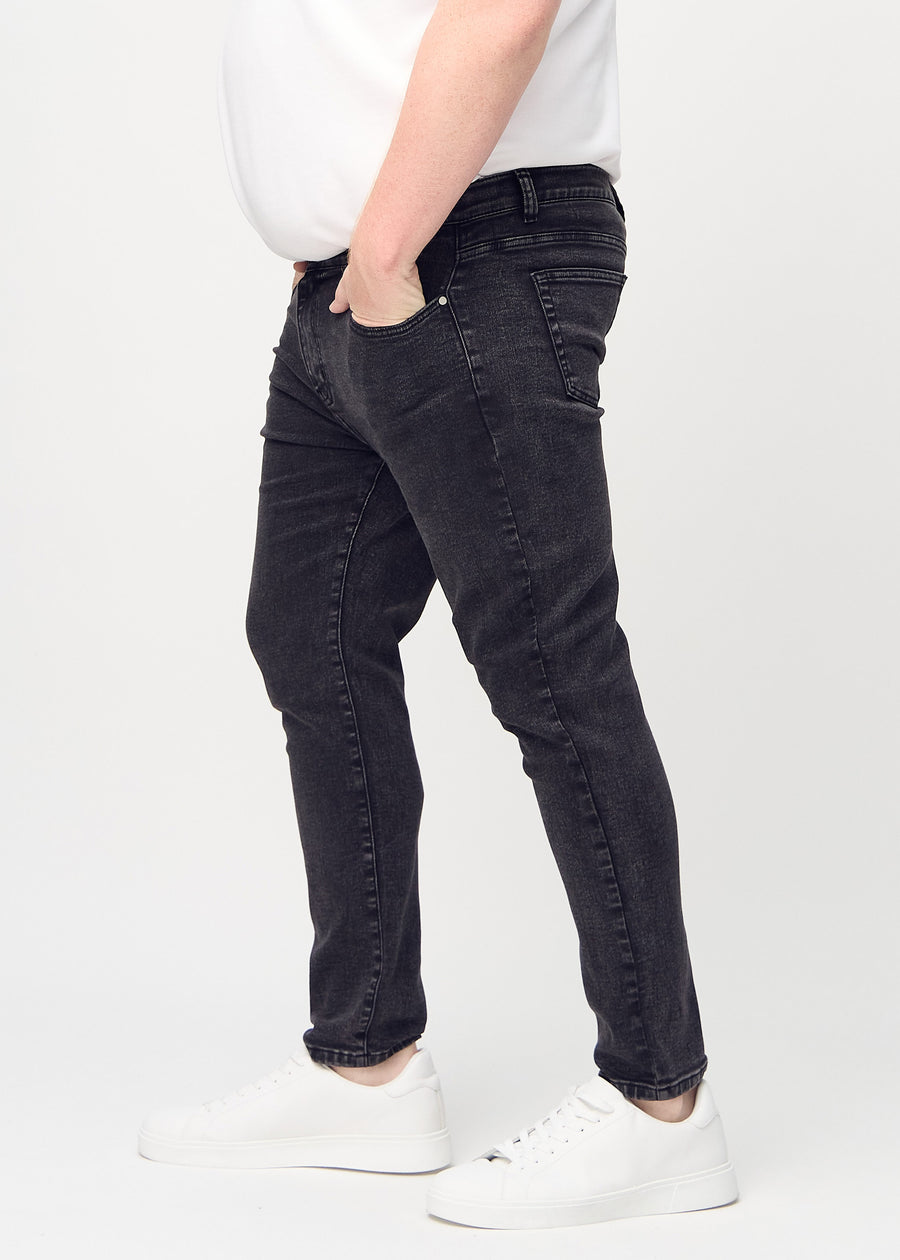 Dark grey denim slim jeans viewed from the side on a plus-size model.