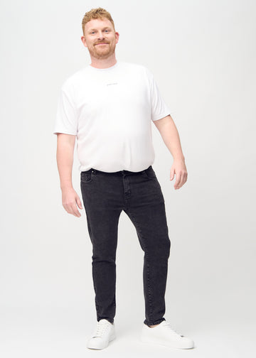 Full-length view of a plus-size model in dark grey denim slim jeans.
