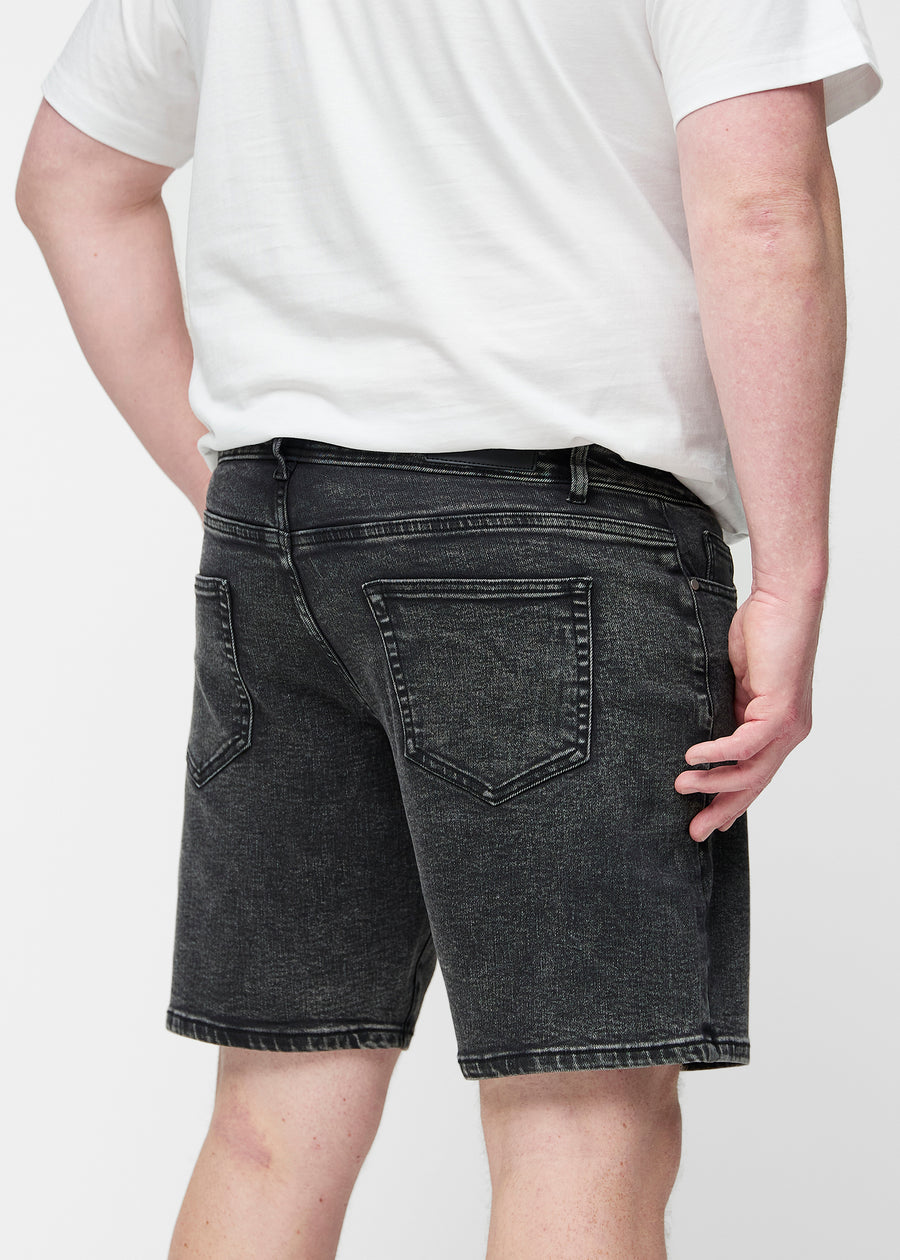 Plus-size model stretches the dark grey denim shorts for men in the colour Shadows at the thigh to show the stretch of the material.