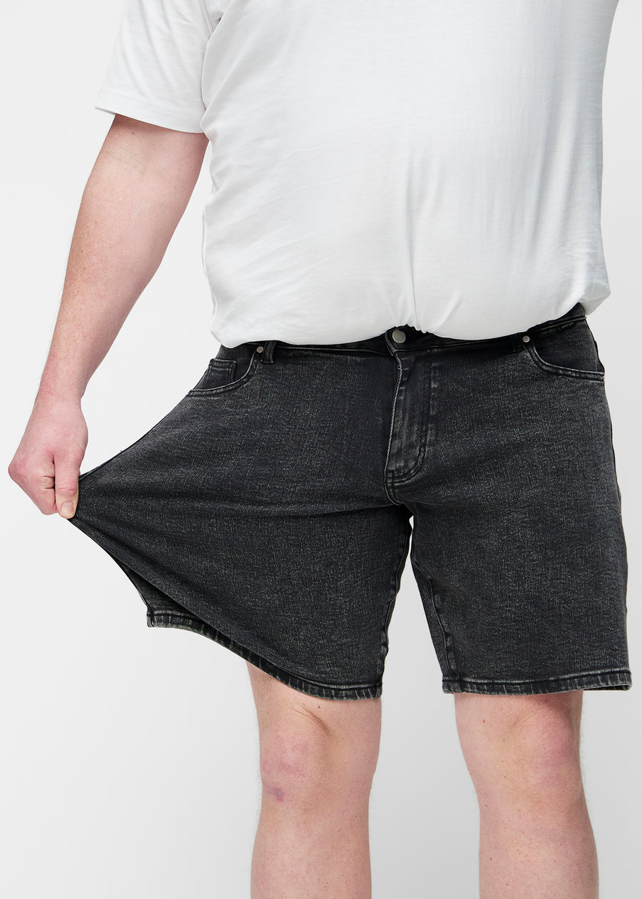 Plus-size model stretches the dark grey denim shorts for men in the colour Shadows at the thigh to show the stretch of the material.
